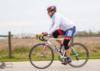 Man riding a bicycle on a paved path during daytime, wearing cycling gear and helmet, promoting Bluebonnet Express.
