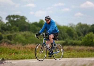 Bicyclist riding a road bike during daytime on scenic route with lush green background.