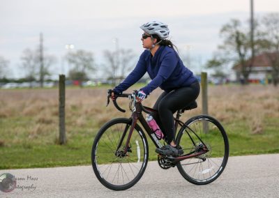 Bright blue and black bicycle on a paved trail during daytime, cyclist wearing helmet and sunglasses.