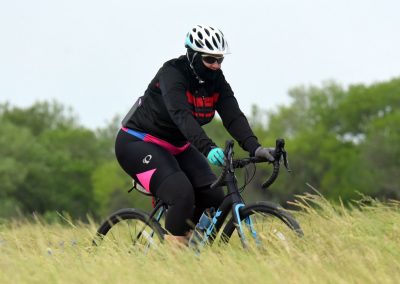 Vibrant cyclist riding a mountain bike through grassy trail, showcasing Bluebonnet Express cycling gear.