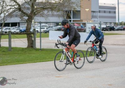 Riders cycling near Bluebonnet Express, urban bike path with parking lot background.