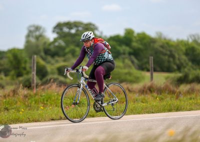Efficient bicycle ride along scenic rural route with cyclist wearing Safety gear, Purple apparel, and a backpack.