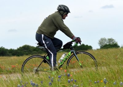 Vast green field with wildflowers, cyclist wearing helmet and riding a mountain bike.