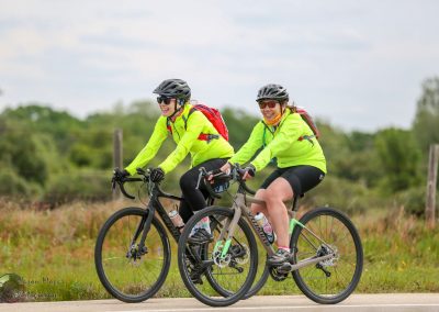 Bright yellow cycling jackets on two women enjoying a ride along the scenic Bluebonnet Express trail.