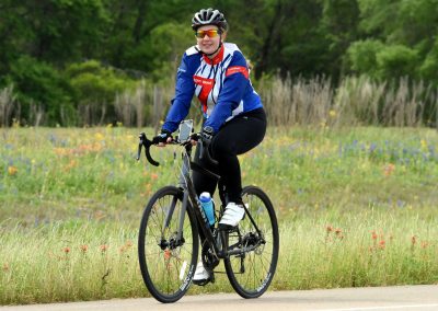 Bright woman cyclist enjoying a ride on Bluebonnet Express trail, surrounded by colorful wildflowers and lush greenery.