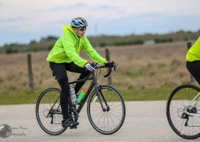 Bright yellow cycling jacket, athletic bike, outdoor rode, overcast sky, active riders, countryside background.