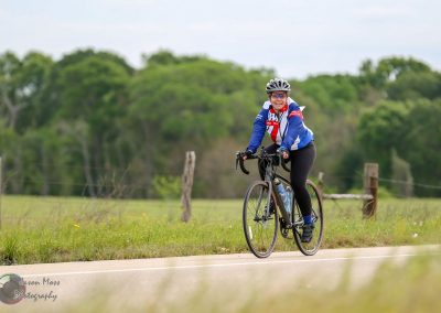 Bright woman cycling on scenic outdoor trail with lush green background, promoting Bluebonnet Express bike tours.
