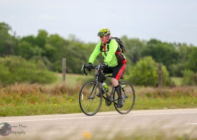 Bicycle rider on scenic rural road with vibrant cycling gear and helmet, enjoying a trail ride.