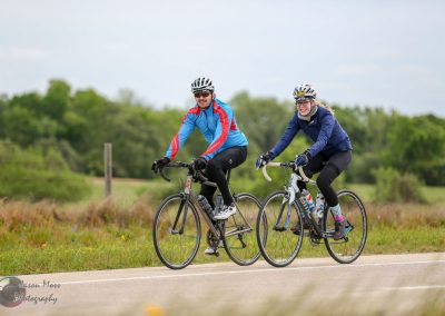 Brightly dressed cyclists riding bikes on scenic countryside trail during daytime.