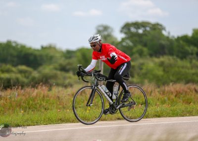 Cyclist in red jersey riding a road bike outdoors during a biking event.
