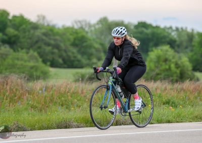 Bright woman cycling on a scenic trail in outdoor sportswear, emphasizing Bluebonnet Express biking experience.