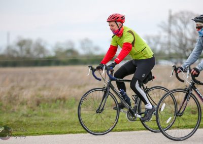 Brightly dressed cyclists riding through open countryside on Bluebonnet Express biking trail.