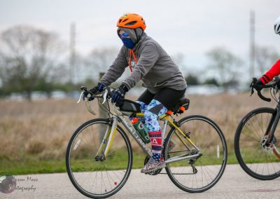 Helmeted cyclist riding a road bike outdoors in cold weather, promoting Bluebonnet Express bike services.