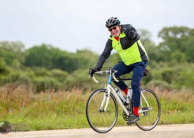 Bright cyclist wearing a helmet, sunglasses, and neon jacket riding a road bike outdoors.