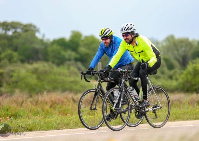 Brightly dressed cyclists riding on scenic route near Texas bluebonnets.