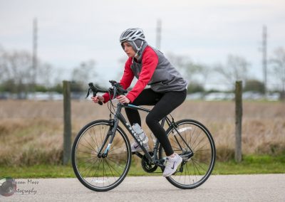 Bright female cyclist riding a Bluebonnet Express bike outdoors in a rural setting.