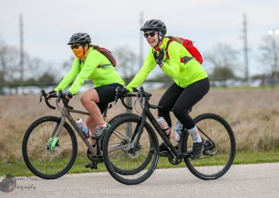 Bright yellow cycling jackets worn by two women riding bikes outdoors for Bluebonnet Express.