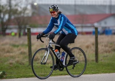 Bright female cyclist riding a road bike on a bike path in outdoor setting.