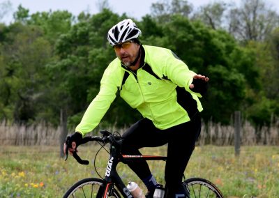 High-visibility cyclist riding through grassy field with trees in background, promoting Bluebonnet Express bike service.