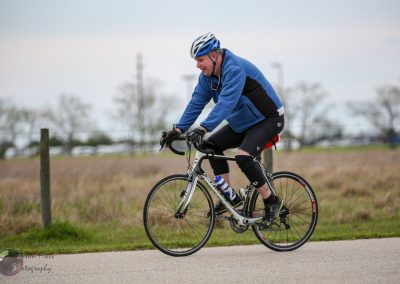 Man riding a road bike outdoors in cooler weather, wearing a blue jacket and helmet.