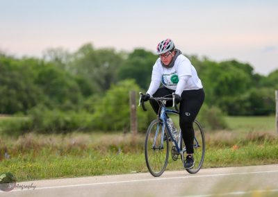 Bright woman cycling on rural road with trees in background, promoting Bluebonnet Express bike service.