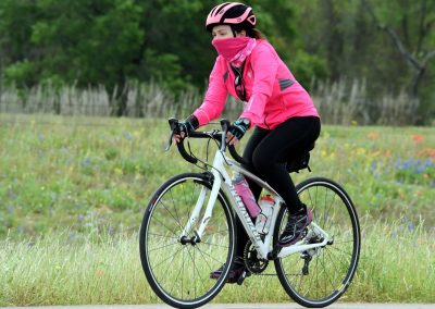 Vibrant pink cycling jacket and helmet on woman riding Bluebonnet Express bike through scenic rural landscape.