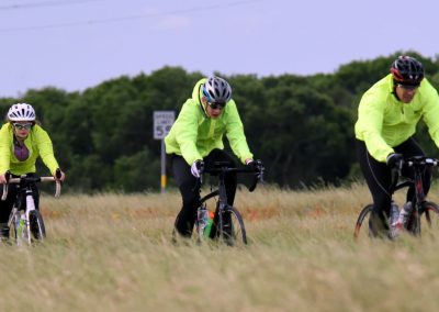 Cyclists riding bikes on grassy field, wearing high visibility jackets, outdoor activity, Bluebonnet Express.