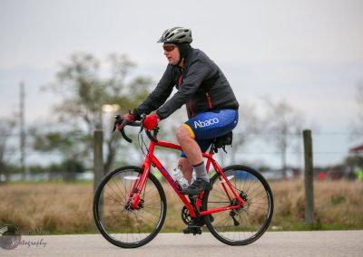 Bright orange road bike with rider in cycling gear, helmets, and sunglasses, promoting Bluebonnet Express bike service.