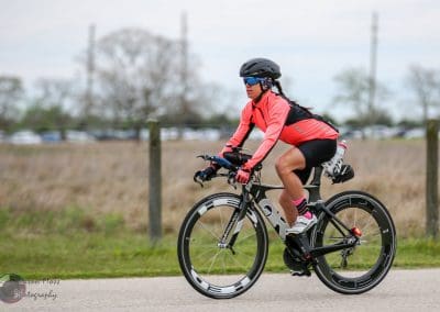 Bright pink and black cycling gear on a woman riding a blue and black road bike outdoors.