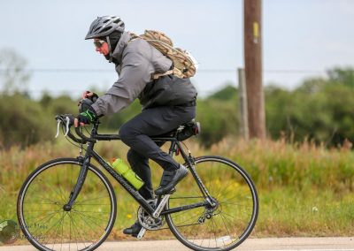 Vibrant cyclist riding a Black Cannondale bike along a rural trail with scenic nature backdrop.