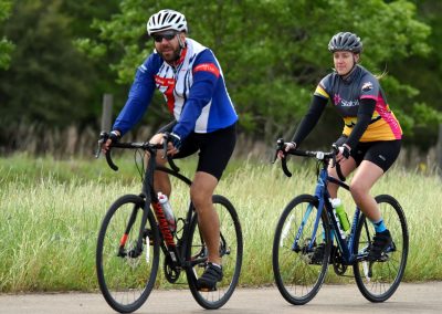 Fast-paced cycling by two bikers on a scenic outdoor trail, promoting Bluebonnet Express bike rides and cycling events.