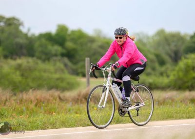 Bright woman cycling outdoors wearing pink jacket and helmet along scenic trail for Bluebonnet Express.