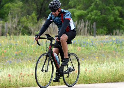 1. Man cycling outdoors on a paved path through a scenic green field with wildflowers.