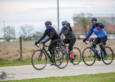 Active cyclists riding their bikes outdoors with masks and helmets on a scenic trail.