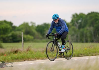 1. Man cycling on road with green fields, wearing blue helmet and cycling gear.