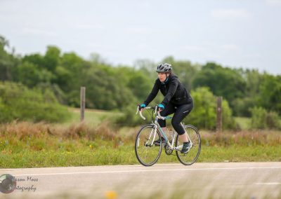 Cyclist riding on scenic outdoor trail with lush green trees and open skies, promoting Bluebonnet Express cycling adventures.