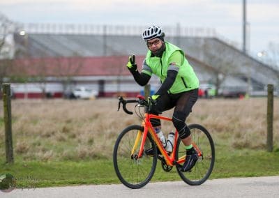 Bright green cycling jersey and helmet on a cyclist riding a road bike outdoors.
