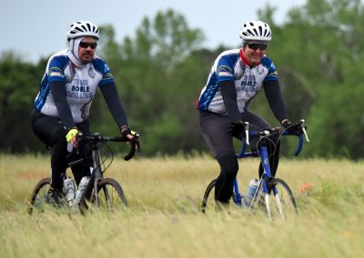 Cycling enthusiasts riding bikes on grassy trail in team jerseys.