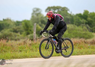 Vibrant cyclist riding on scenic countryside route with lush greenery and flowers.