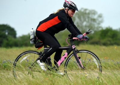 Vibrant woman cyclist riding a sports bike outdoors in grassy field with colorful wildflowers.