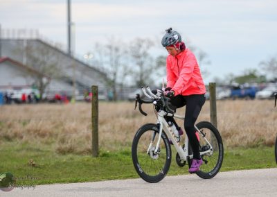Woman riding electric bicycle outdoors during daytime, wearing helmet and sportswear for eco-friendly commuting.