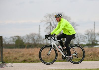 Bright yellow cycling jacket with man riding a Trek bike on a rural road, promoting eco-friendly transportation.