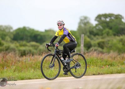 Vibrant female cyclist enjoying a scenic ride on a black bike with Bluebonnet Express jersey.