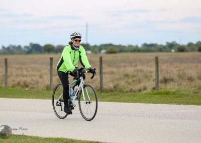 Woman cycling outdoors in bright green jacket on a paved rural road during daytime.