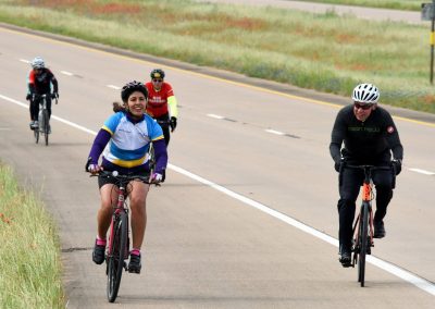 Cyclists riding on a scenic rural highway during daytime, promoting outdoor biking and community recreation.