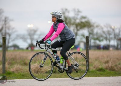 Cyclist riding a bike outdoors with a scenic background, promoting Bluebonnet Express cycling events.