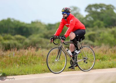 Vibrant cyclist riding a bike outdoors with lush greenery, promoting Bluebonnet Express cycling event.