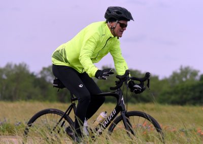 Vibrant cyclist wearing a neon yellow jacket riding a mountain bike through grassy fields during daytime.