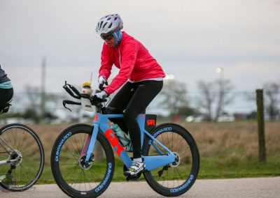 Vibrant blue and red bike for Bluebonnet Express race, ridden by cyclist with pink jacket and helmet, during a cycling event.