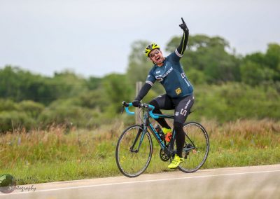 Vibrant cyclist celebrating victory on scenic outdoor bike route during daytime.